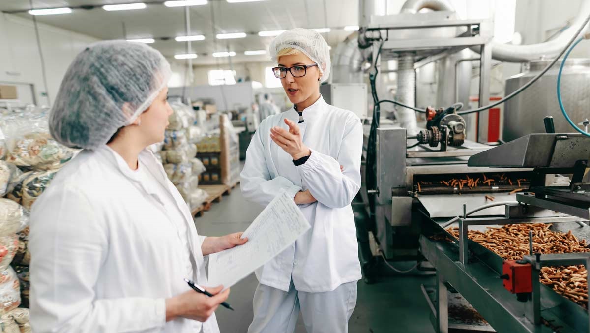 Food manufacturing workers talking to each other in food packing facility.